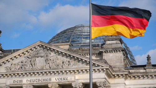 Foto des Reichstagsgebäudes mit der deutschen Fahne im Vordergrund