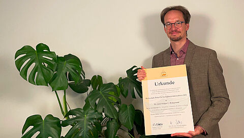 Das Foto zeigt den Preisträger Dr. Holger Bringmann mit der Urkunde des Holzschuh-Preises 2022.